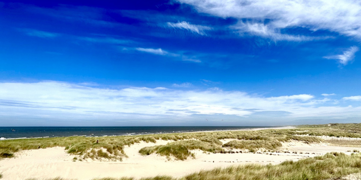Die Hälfte des Bildes nimmt der blaue Himmel mit Schleierwolken ein. Die anderen Hälfte zeigt hellen Dünensand mit Strandhafer.