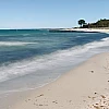 Langzeitaufnahme der Ostsee im linken Teil des Bildes, rechts Sandstrand, Bäume und Büsche am Horizont.