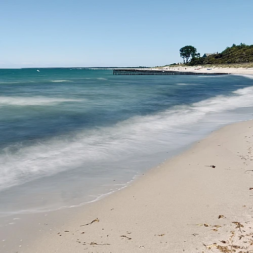 Langzeitaufnahme der Ostsee im linken Teil des Bildes, rechts Sandstrand, Bäume und Büsche am Horizont.
