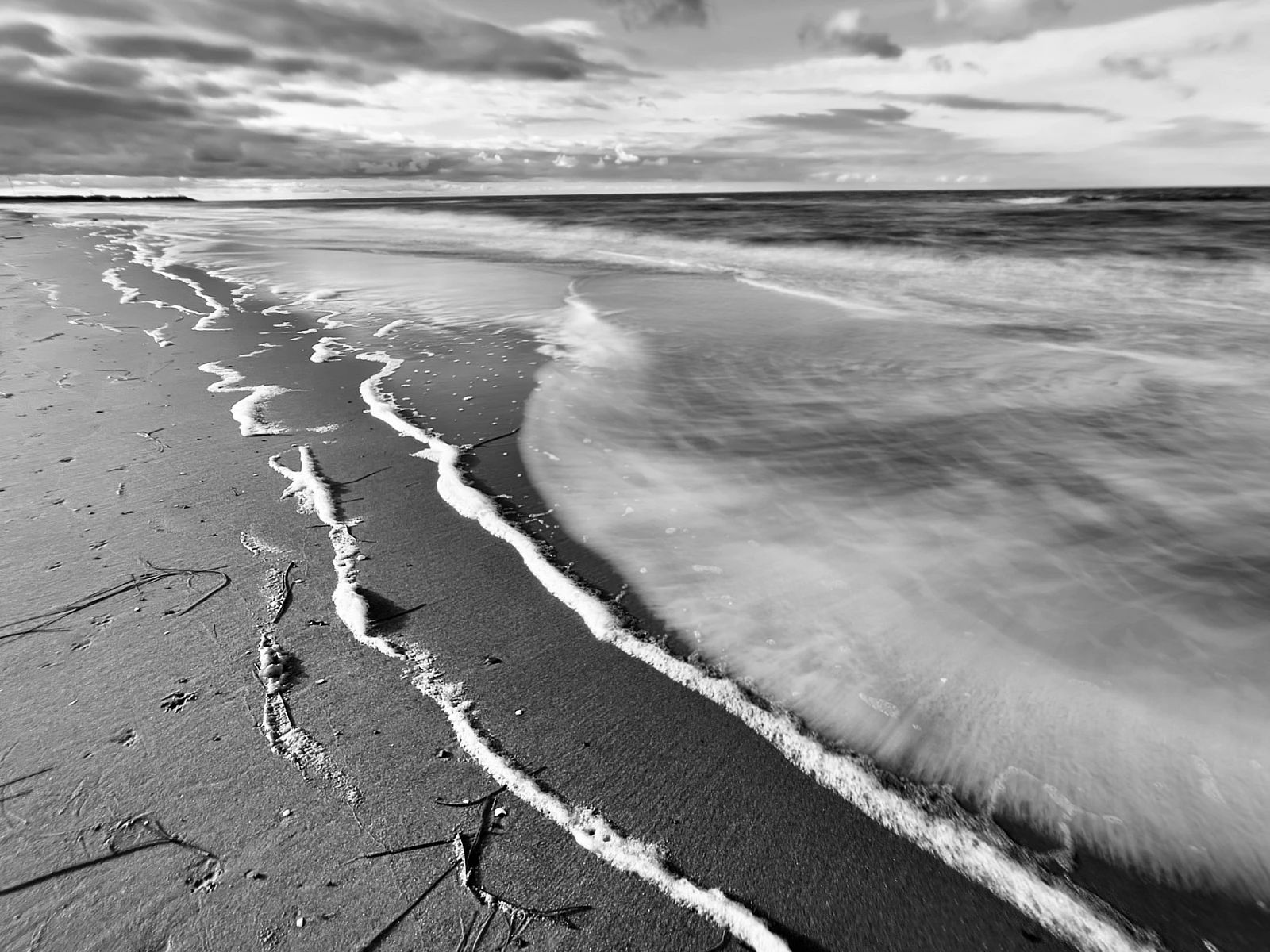 Schwarzweiß-Aufnahme der Ostsee. Meeressaum mit Schaum vor dem verwaschenen Meer.