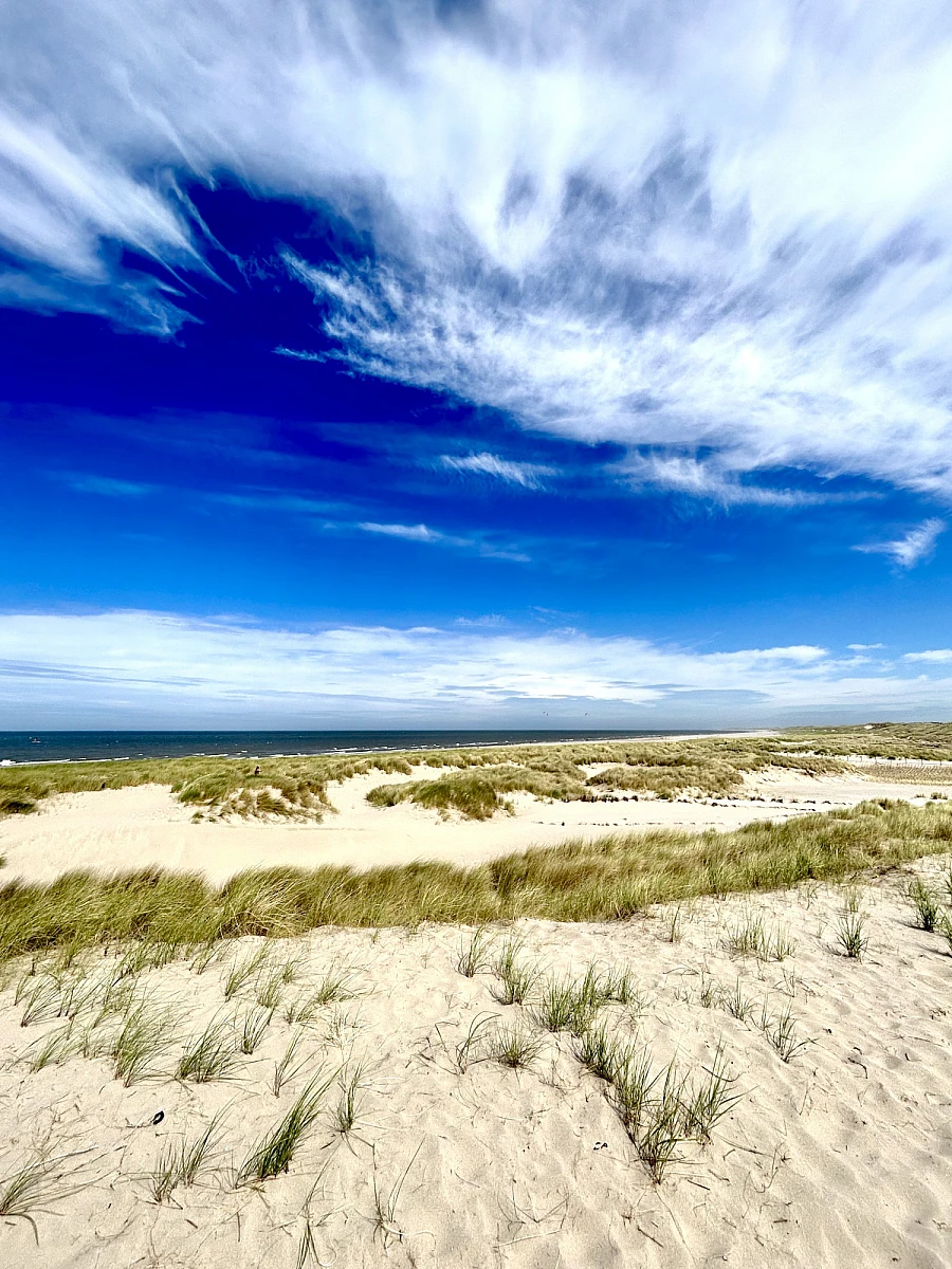 Im oberen Drittel des Bildes Himmel mit weißen Wolken, die folgenden zwei Drittel: nasser Strand auf dem sich der Himmel spiegelt.