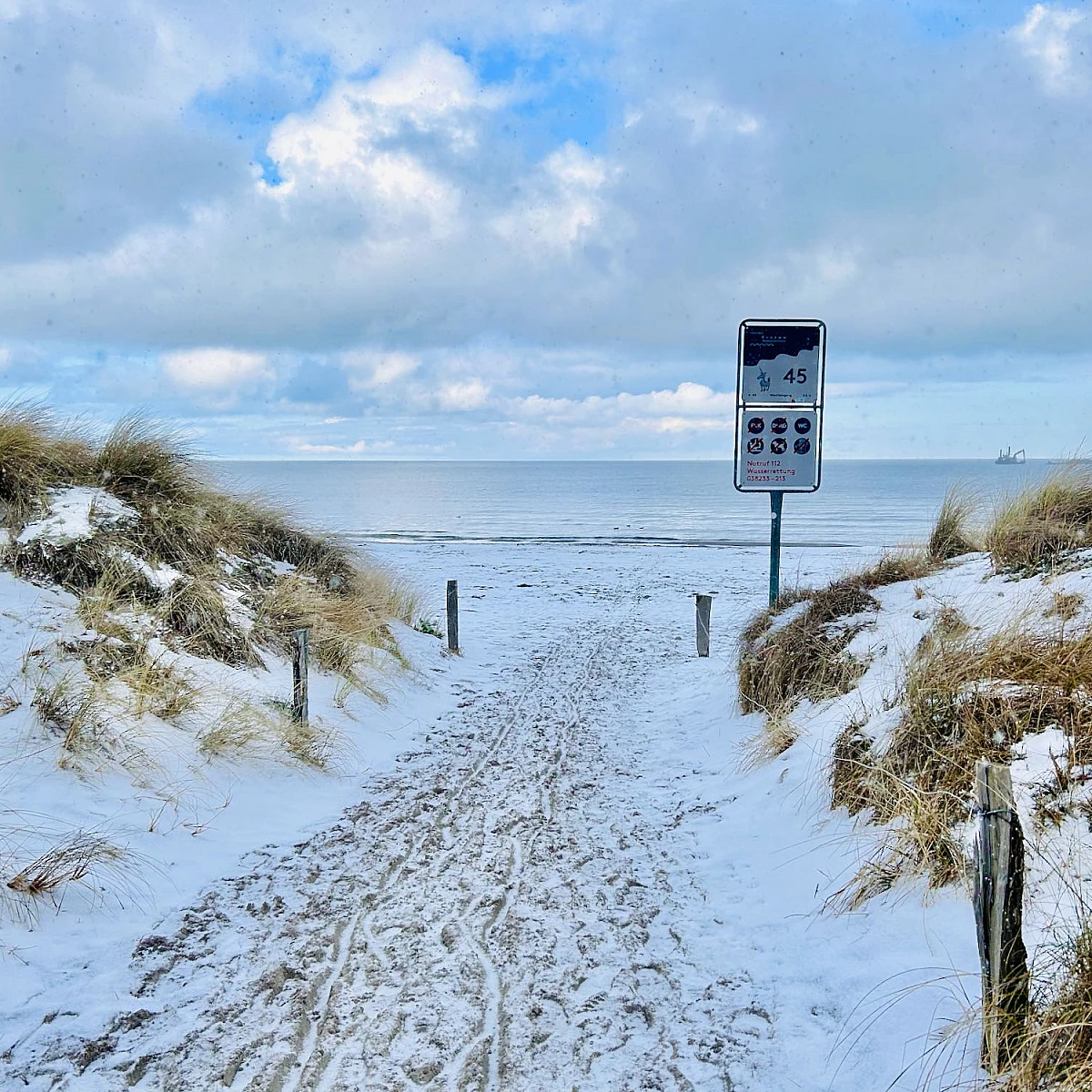 Blick auf die Ostsee durch einen Strandzugang. Es liegt leichter Schnee, der Himmel ist wolkenverhangen.