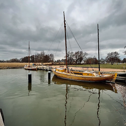 Ein Zeesboot liegt im Wecker Hafen. Der Himmel ist wolkenverhangen.