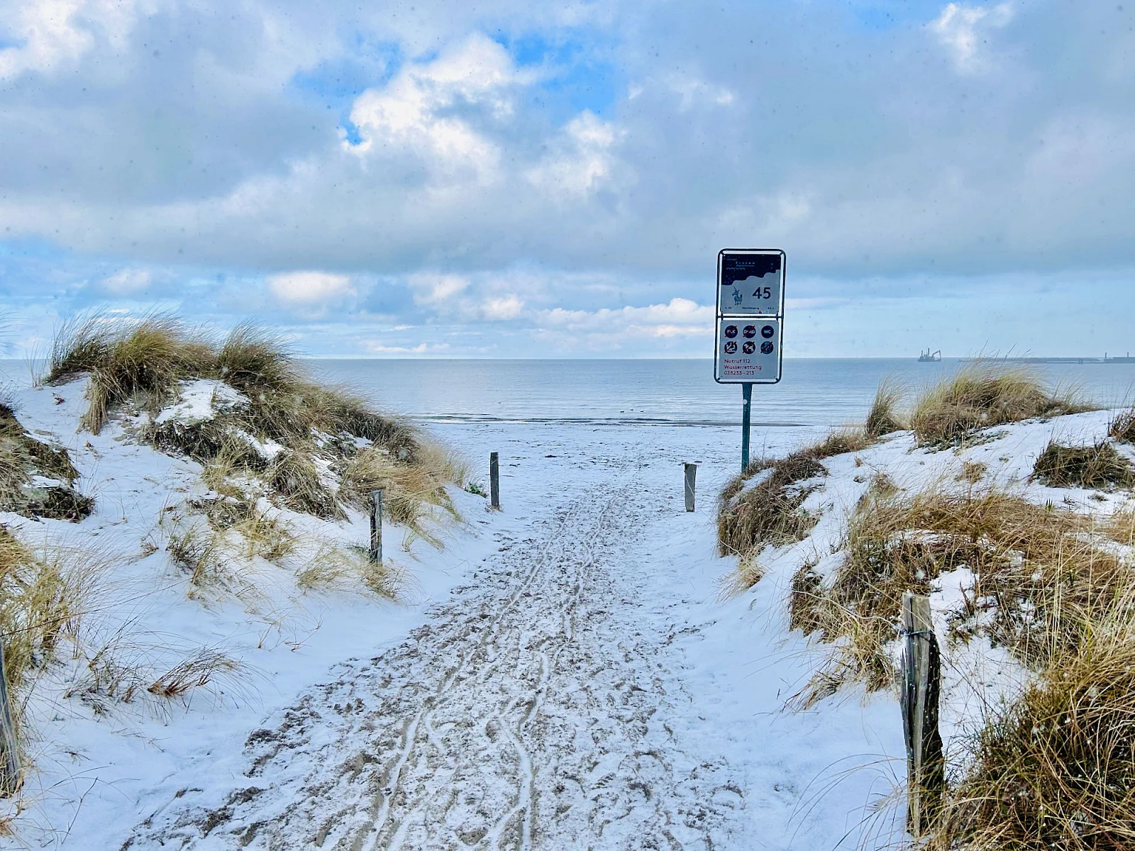 Blick auf die Ostsee durch einen Strandzugang. Es liegt leichter Schnee, der Himmel ist wolkenverhangen.