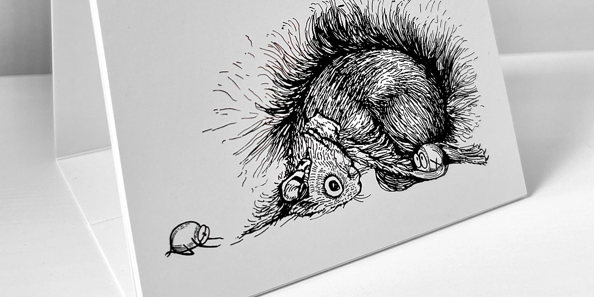 Der Kalender steht aufgeklappt auf einer weißen Fläche. Es ist der Monat Februar zu sehen. Es ist eine Illustration zu sehen, auf der ein Eichhörnchen und zwei Haselnüsse in der Kindspose verweilen.
