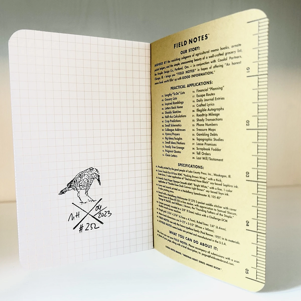 Foto eines stehenden und aufgeklappten Field Notes Heftes. Auf der linken Seite ist der Stempel auf kariertem Papier zu sehen.