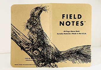 Foto eines aufgeklappten Field Notes Heftes mit Kraft-Papier-Deckel. Die Zeichnung erstreckt sich über den gesamten Buchdeckel und zeigt die detaillierte Illustration eines Eichhörnchens, das auf einem Ast sitzt und aufmerksam aufrecht sitzend nach links schaut.