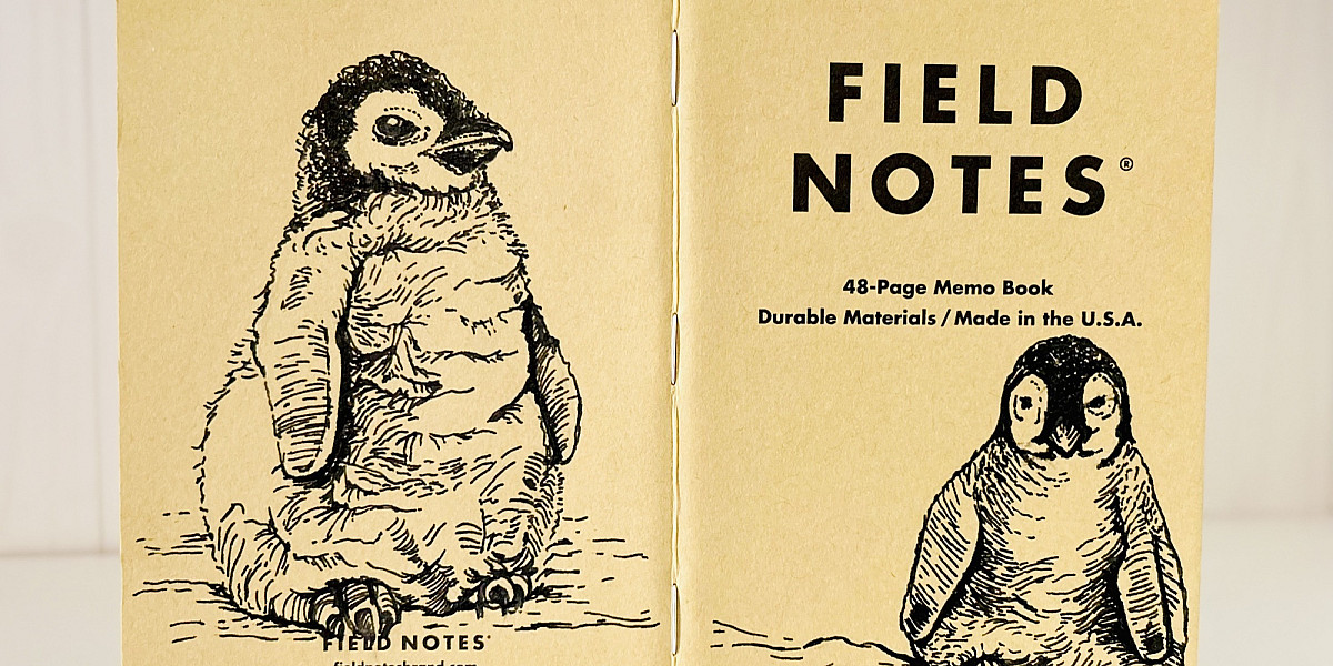 Foto eines aufgeklappten Field Notes Heftes mit Kraft-Papier-Deckel. Auf Rücken und Cover befindet sich jeweils eine schwarze Zeichnung eines sitzenden Baby Pinguins.