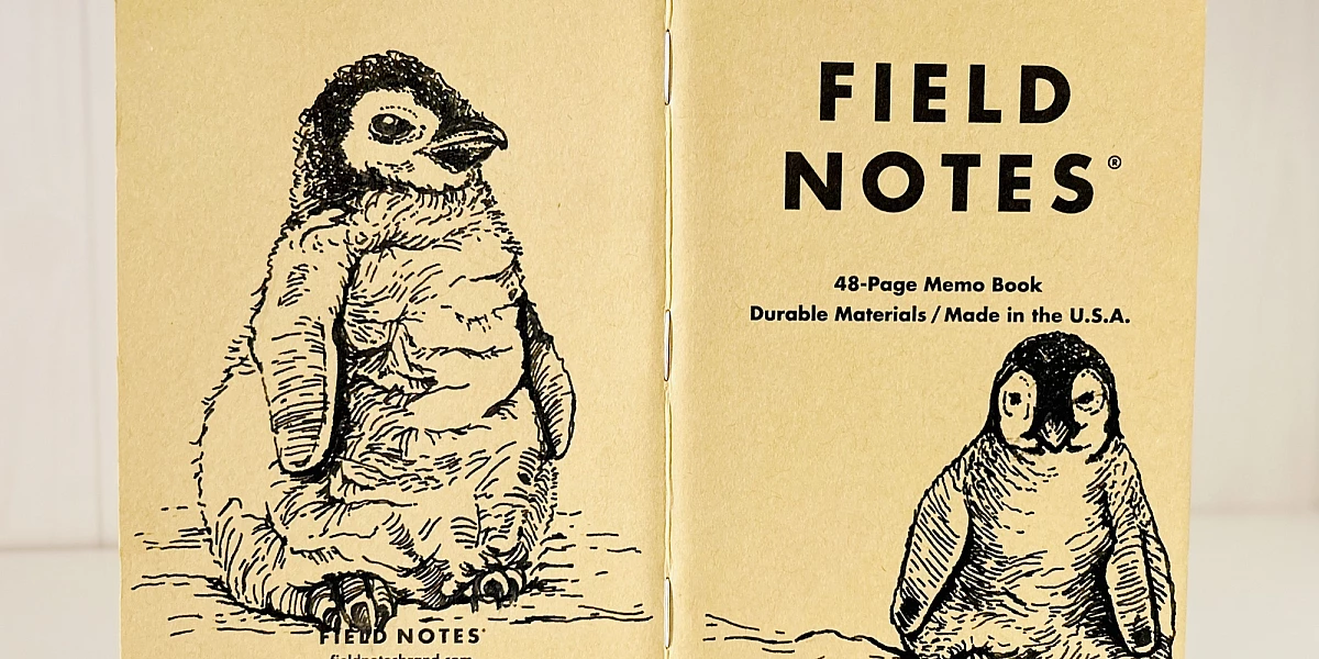 Foto eines aufgeklappten Field Notes Heftes mit Kraft-Papier-Deckel. Auf Rücken und Cover befindet sich jeweils eine schwarze Zeichnung eines sitzenden Baby Pinguins.