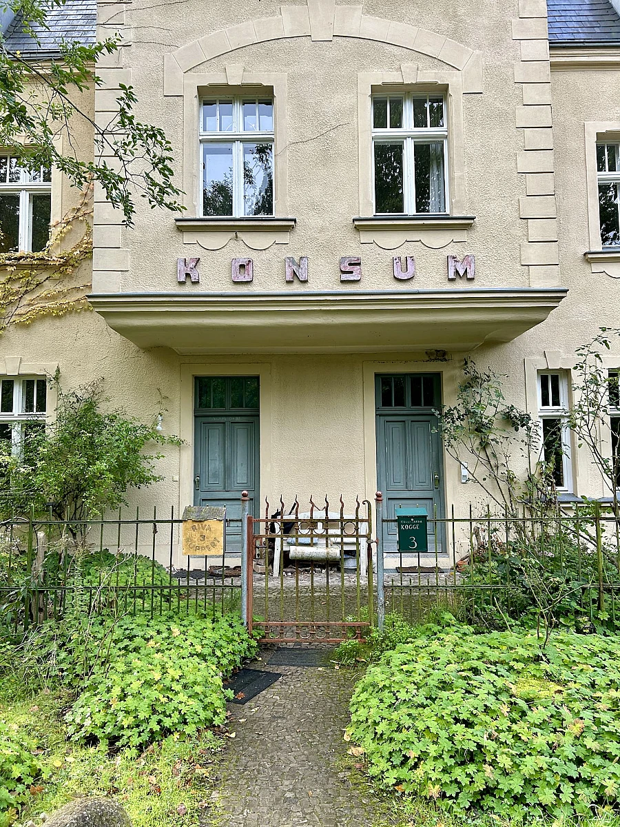 Das Foto eines Hauseingangs über dem "Konsum" steht.