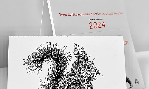 Der Kalender "Ommmmmmmmmmmm - Yoga für Eichhörnchen & ähnlich veranlagte Menschen - Postkartenkalender 2024"  steht aufgeklappt auf einer weißen Fläche. Im Vordergrund eine abgetrennte Postkarte.