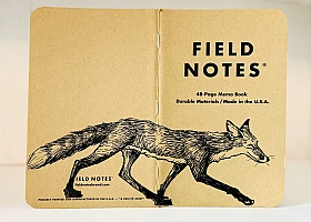 Auf dem aufgeklappten Rücken eines Field Notes Heftes ist eine schwarze Tintezeichnung eines Fuchses zu sehen. Der sehr schlanke Fuchs läuft von links nach rechts.