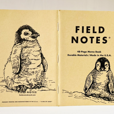 Foto eines aufgeklappten Field Notes Heftes mit Kraft-Papier-Deckel. Auf Rücken und Cover befindet sich jeweils eine schwarze Zeichnung eines sitzenden Baby Pinguins.
