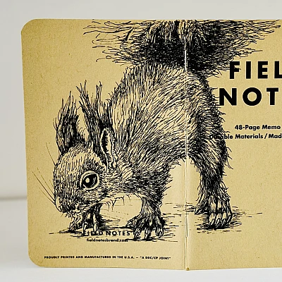 Ein aufgeklapptes Field Notes Heft auf dessen Rücken aus Kraft-Papier sich die Zeichnung eines Eichhörnchens befindet.
