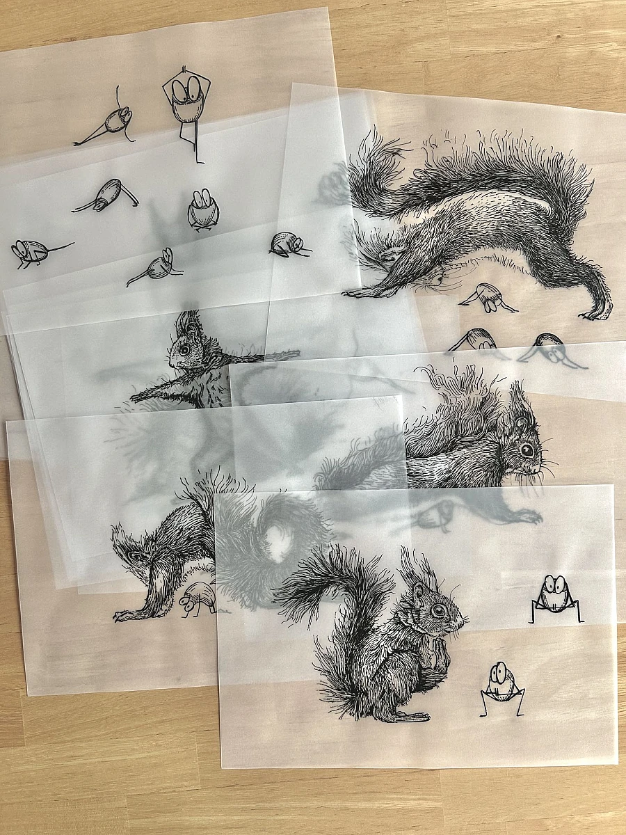 Vier Blätter Transparentpapier mit Tintezeichnungen liegen übereinander auf einem Holztisch. Links oben ein Hahnemühle Entwurfsblock.