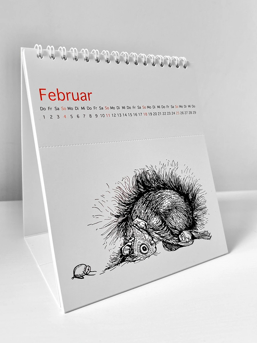 Der Kalender Ommmmmmmmmmmm - Yoga für Eichhörnchen & ähnlich veranlagte Menschen - Postkartenkalender 2024  steht seitlich aufgeklappt auf einer weißen Fläche. Auf dem Cover ist ein Eichhörnchen zu sehen, das die Position des herabschauenden Hundes praktiziert.  Fünf Haselnüsse praktizieren ebenfalls Yoga.
