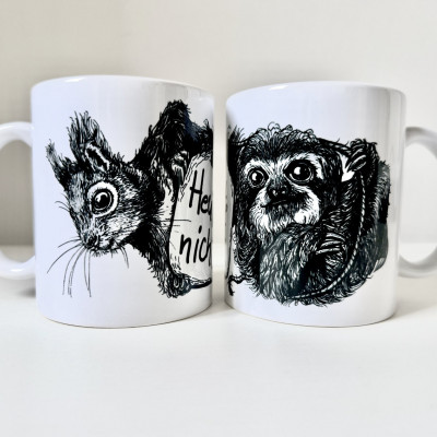 Zwei weiße Keramiktassen stehen nebeneinander. Auf der linken Tasse die schwarze Zeichnung eines Eichhörnchenkopfes, auf der rechten die schwarze Zeichnung eines Faultiers.