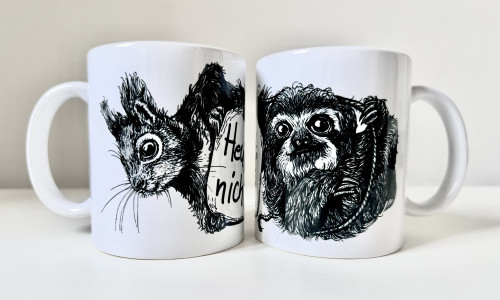 Zwei weiße Keramiktassen stehen nebeneinander. Auf der linken Tasse die schwarze Zeichnung eines Eichhörnchenkopfes, auf der rechten die schwarze Zeichnung eines Faultiers.