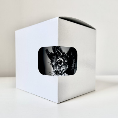Ein weißer Karton mit Sichtloch. Dahinter auf der sich darin befindenden Tasse die schwarze Zeichnung eines Eichhörnchenkopfes.